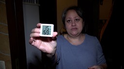 Angela Caci Grillo in ihrer Wohnung, zeigt ein Termometer in die Kamera. Es zeigt 15.4 Grad Celsius an.