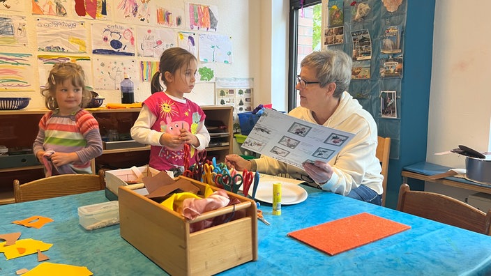 Eine Erzieherin wie sie mit zwei Kindern bastelt.