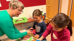 Claire Herzog wie sie mit zwei Kindern Pappe zum basteln schneidet.