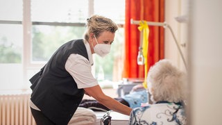 Eine Pflegekraft mit Maske schaut in einem Patientenzimmer nach einer Seniorin