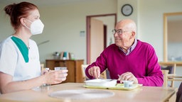 Eine Pflegerin sind mit einem älteren Herren an einem Essenstisch