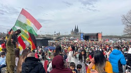 Menschen schwenken vor der Kulisse des Kölner Doms kurdische und deutsche Fahnen