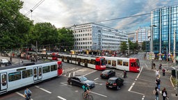 Eine Kreuzung in einer Großstadt mit viel Verkehr. Kraftfahrzeuge und Straßenbahn, sowie Radfahrer und Fußgänger sind unterwegs.