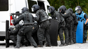 Mehrere Polizisten in Uniform und Schutzhelm verstecken sich hinter einem weißen Transporter. (Symbolfoto)