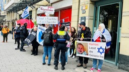 Rund 20 Menschen demonstrieren vor einer Häsuerreihe am Kölner Neumarkt, eine Demonstrantin hält ein Schild mit Kritik an der Hamas