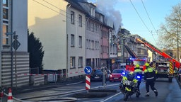 Aus einem Haus kommt Rauch. Auf der STarße steht ein Polizeimotorrad und ein FEuerwehrauto.