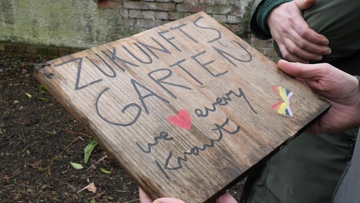 Zu sehen ist ein Holzschild mit der Aufschrift "Zukunftsgarten - we love every Kraut" 