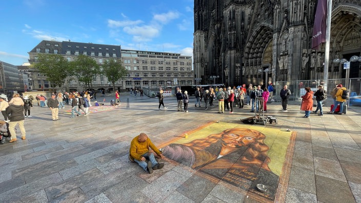 Ein Straßenmaler vor dem Dom malt an einem Jesus-Bild.