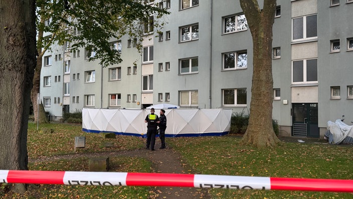 Polizisten stehen vor einem aufgestellten Zelt vor einem Wohnhaus. 