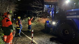 Das THW räumt mit schwerem Gerät Bäume und Dachteile von der Straße im Kölner Süden.