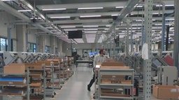 Das Bild zeigt eine Große Halle in der Elektrotechnik produziert wird und ein Mann in einem Kittel arbeitet.