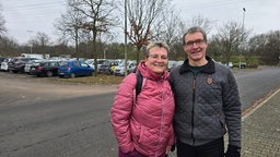 Mann und Frau stehen vor einem großen Parkplatz 