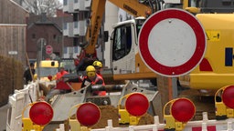 Im Vordergrund steht ein "Durchfahrt verboten"-Schild und im Hintergrund sind Bauarbeiter, welche arbeiten.