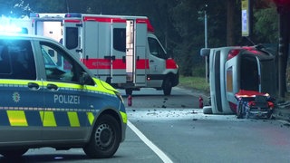 Polizei und Rettungswagen, das Unfallfahrzeug liegt mit zersörtet Heckscheibe auf der Beifahrerseite