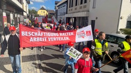 ZF-Mitarbeiter laufen bei einer Demo gegen die Werksschließungen durch die Straßen. Sie halten Banner in die Höhe. Im Vordergrund steht auf einem Banner: "Beschäftigung halten. Arbeit verteilen."