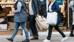 Menschen mit Taschen in der Fußgängerzone vor Geschäften