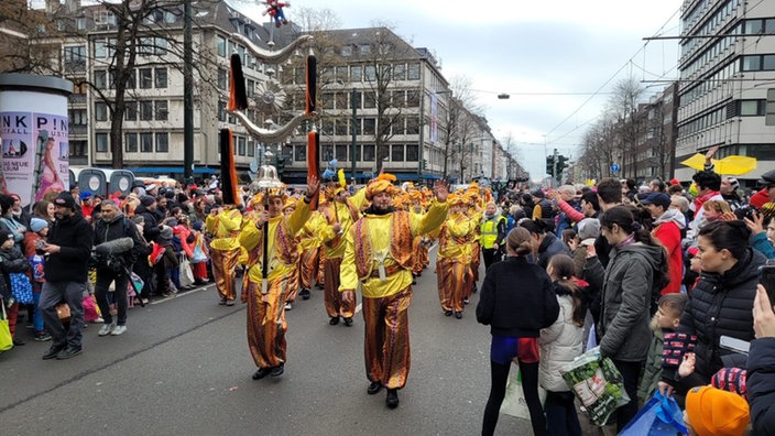 Der Düsseldorfer Zoch ist unterwegs! Mit dem Spielmanns- und Fanfarenzug Kolping aus dem münsterländischen Metelen an der Spitze. Die Zuschauer stehen dicht gedrängt in 4er- und 5er-Reihen an der Strecke.