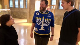 Ein Mann steht in der Alten Synagoge in Essen und hat einen Chanukka-Pulli an.