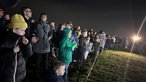 Zuschauer stehen auf einer Wiese. 