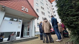 Gruppe von Menschen stehen vor Hochhaus mit Gepäck