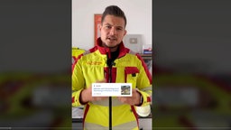 Junger Mann in Rettungsdienst-Uniform warnt vor klettern auf den Waggons.