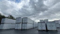 Mehrere graue Schiffscontainer nebeneinander gestapelt. 