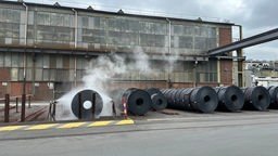 Stahlrollen auf dem Werksgelände, dahinter ein Industrie-Gebäude