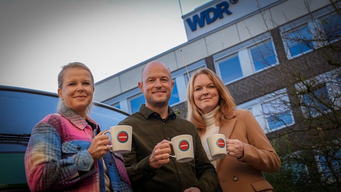 Unsere drei Moderatoren posieren mit einer Lokalzeit-Tasse vor einem Bulli und dem WDR-Landesstudio Dortmund und wollen sich von einer Tasse zu einer Sensation hochtauschen