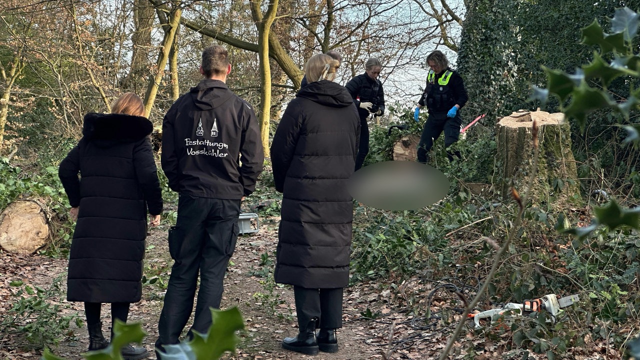 Polizisten und andere Personen stehen in einem Waldstück.