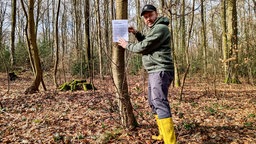 Naturschützer Martin Maschka hängt in einem Wald in Wetter Hinweisschilder zur Salamanderpest auf