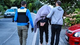 Zwei Polizisten führen einen Mann in Handschellen ab