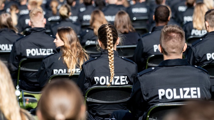 Polizeiabzeichen im Vordergrund und verschwommene Polizeischüler im Hintergrund