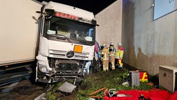 Die Unfallstelle in Kleve. Das stark beschädigte und verdrehte Führerhaus des Lkws steht vor einem Gebäude. Zwischen Lkw und Wand ist der eingedrückte Kleinbus zu sehen. Darum stehen Einsatzkräfte.