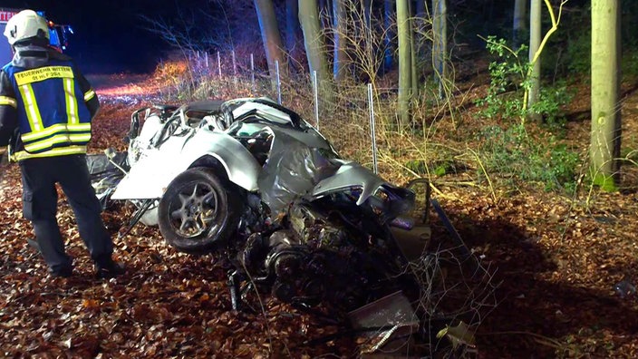 Ein Feuerwehrmann steht mit dem Rücken zur Kamera neben einem komplett zerstörten Auto