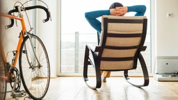 junger Mann im Schaukelstuhl, Rennrad im Zimmer 