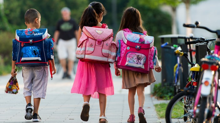 Drei Schulkinder mit Schulranzen auf ihrem Weg zur Schule.