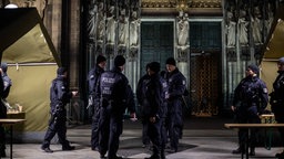 Polizisten stehen neben Zelten, wo Besucher und Teilnehmer der Messe kontrolliert werden