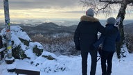 Zwei Personnen schauen sich die Schneebedeckte Landschaft an