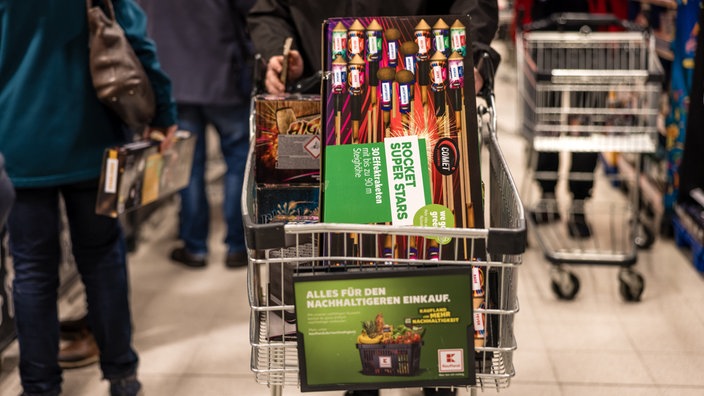 Ein Kunde fährt mit einem Einkaufswagen voller Feuerwerk durch einen Supermarkt. 