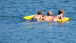 Drei Badegäste schwimmen mit einer Luftmatratze über einen Badesee