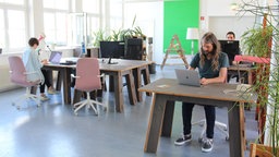 Menschen sitzen an Bürotischen in einem großen Raum