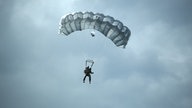 Ein Polizist einer Spezialeinheit gleitet mit einem Fallschirm vor bewölktem Himmel (Symbolbild)