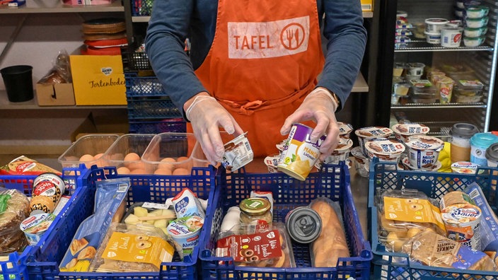 Ein ehrenamtlicher Helfer der Tafel packt Lebensmittel in Plastikboxen. 