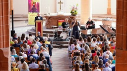 Eine Band spielt in einer Kirche vor vielen Besuchern, die auf Stühlen sitzen