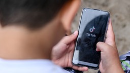 Ein Junge hält ein Smartphone in der Hand, auf dem das TikTok Logo zu sehen ist