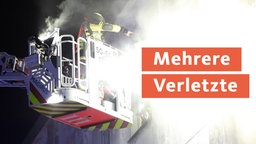 Ein Feuerwehrmann steht auf einem Rettungskran und löscht einen Hausbrand 