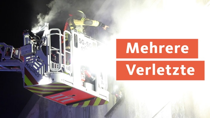 Ein Feuerwehrmann steht auf einem Rettungskran und löscht einen Hausbrand 