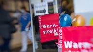 Rote Plakate mit der Aufschrift "Heute Warnstreik" hängen vor den Fenstern einer Klinik