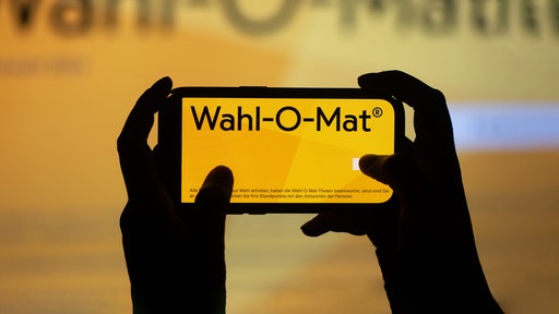 Zwei Hände halten ein Handy mit dem Wahl-O-Mat-Logo auf dem Bildschirm