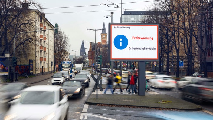 Befahrene Straße mit Schild, auf dem steht "Amtliche Warnung. Probealarm. Es besteht keine Gefahr."